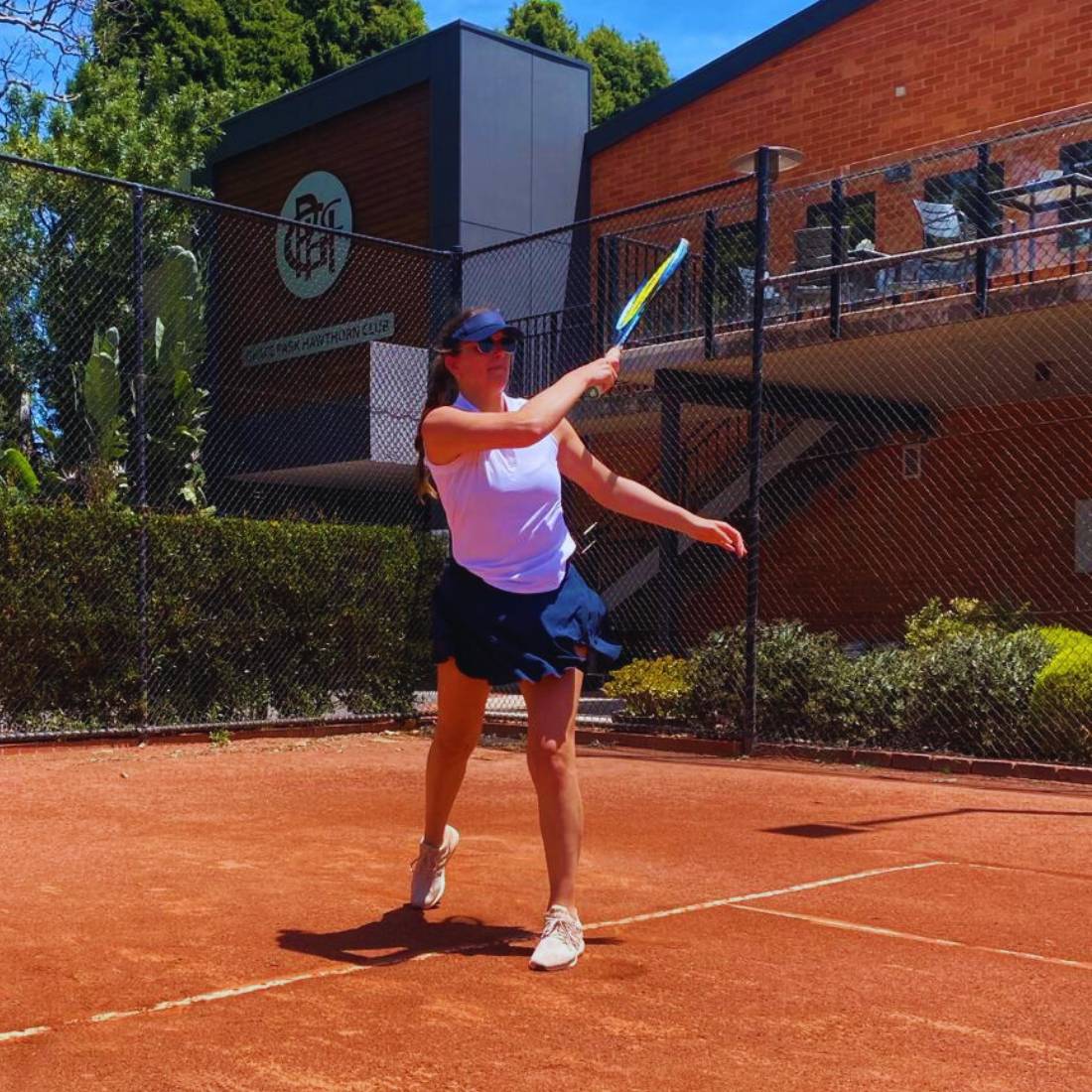 Woman in sportswear playing tennis on a clay court during the day.